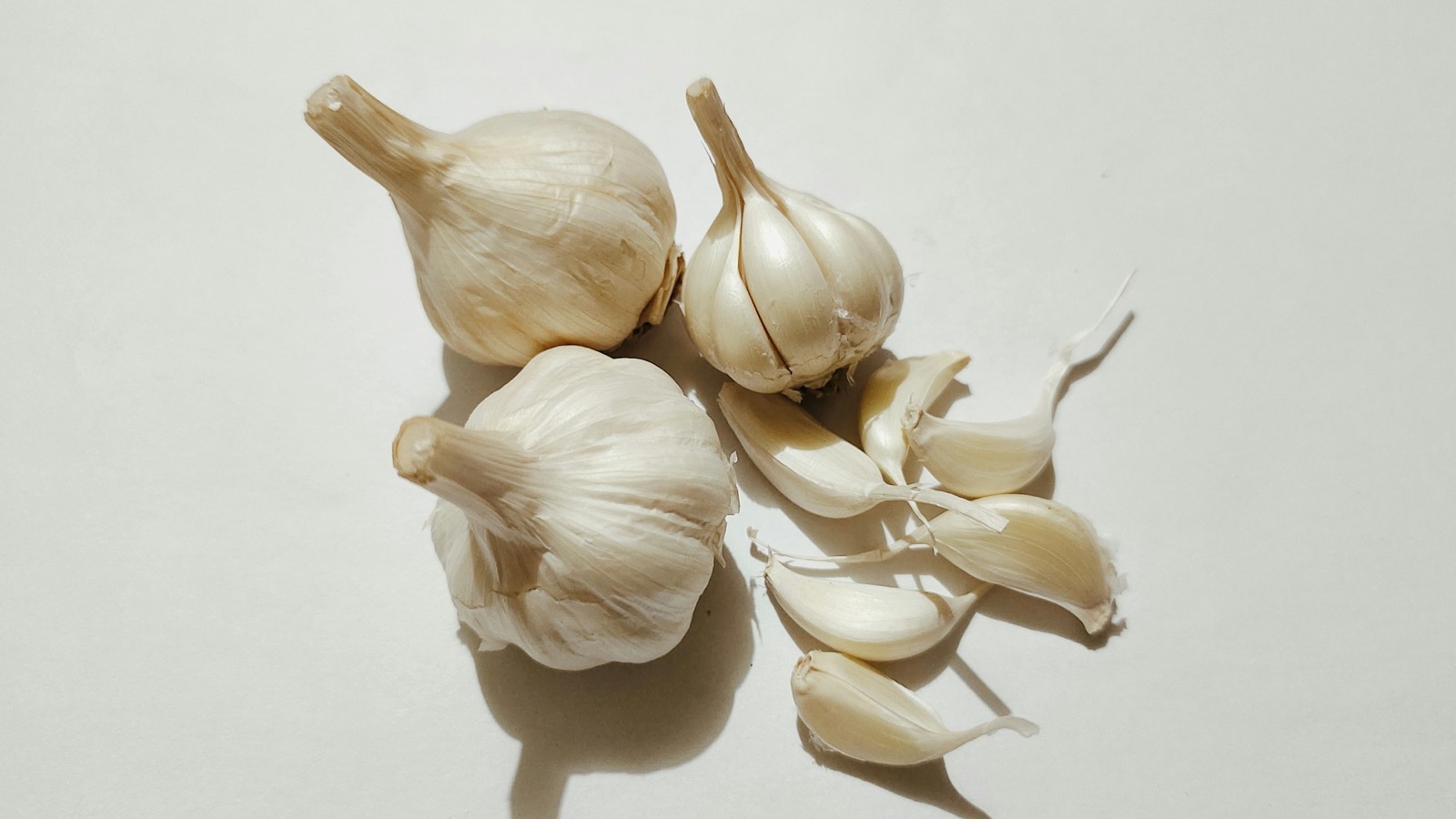 Whole garlic bulbs and loose cloves on a warm neutral background